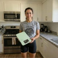 Woman in kitchen holding a digital scale. ScaleMyPlate